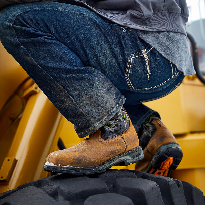 Person wearing work boots and jeans sitting on a piece of heavy machinery.