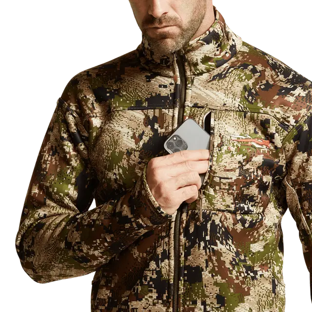 Person wearing a camouflage jacket holding a phone with a white background