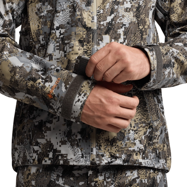 Close-up of a person wearing a camouflage jacket with a focus on the sleeve and hand.