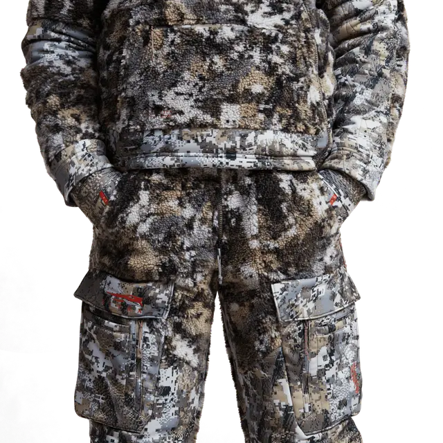 Man wearing camouflage bibs with Sitka brand on a white background