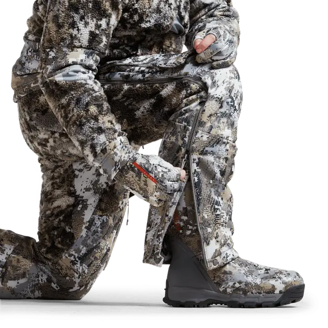 Man wearing camouflage bibs with Sitka brand on a white background