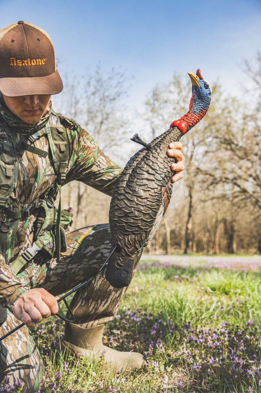 Hunter holding a turkey decoy in a natural setting with trees and grass.