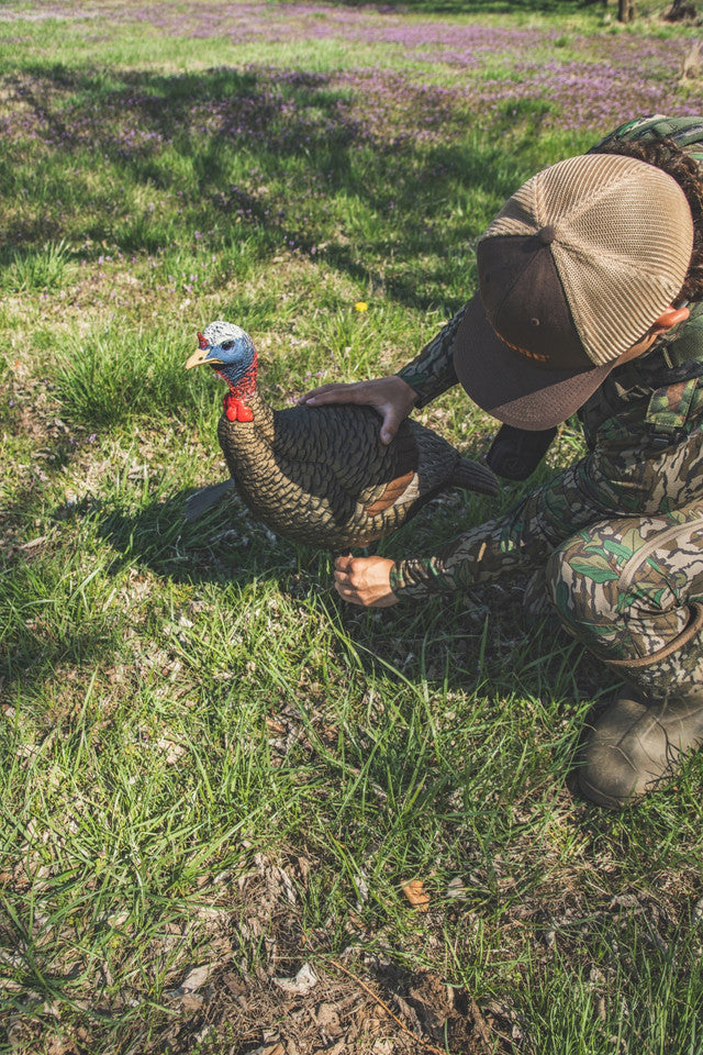 Person in camouflage gear interacting with a turkey in a grassy field