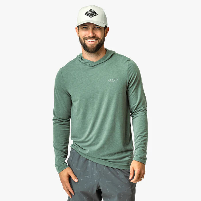 Man wearing a green long-sleeve shirt and gray shorts with a white cap on a white background