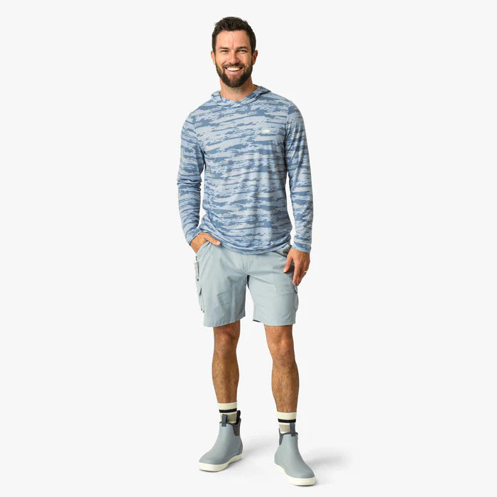Man wearing a blue patterned long-sleeve shirt and light gray shorts on a white background