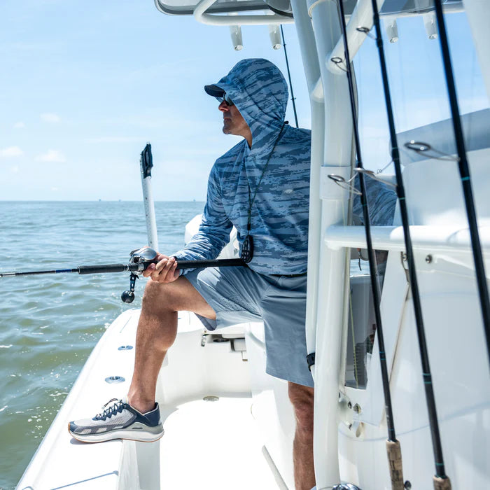 Man fishing on a boat wearing a blue camouflage hoodie and gray shorts.