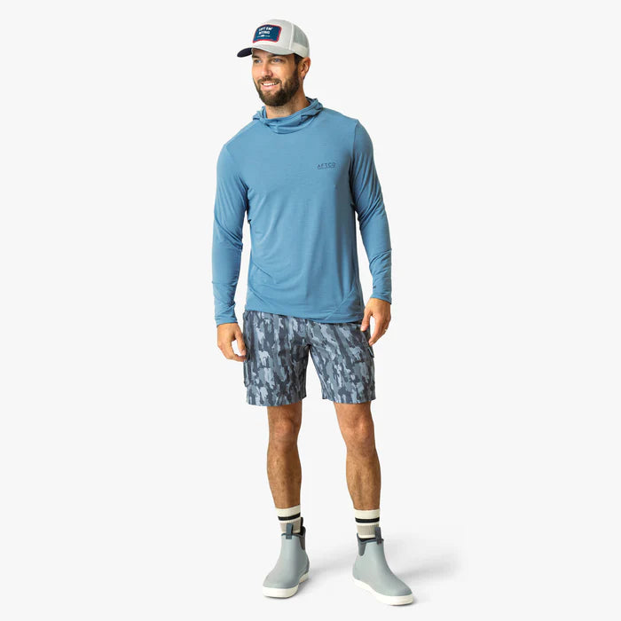 Man wearing a blue long-sleeve shirt, camouflage shorts, and gray shoes on a white background