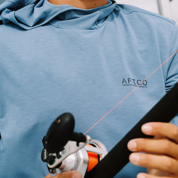 man wearing blue hoodie with brand logo while holding a fishing rod
