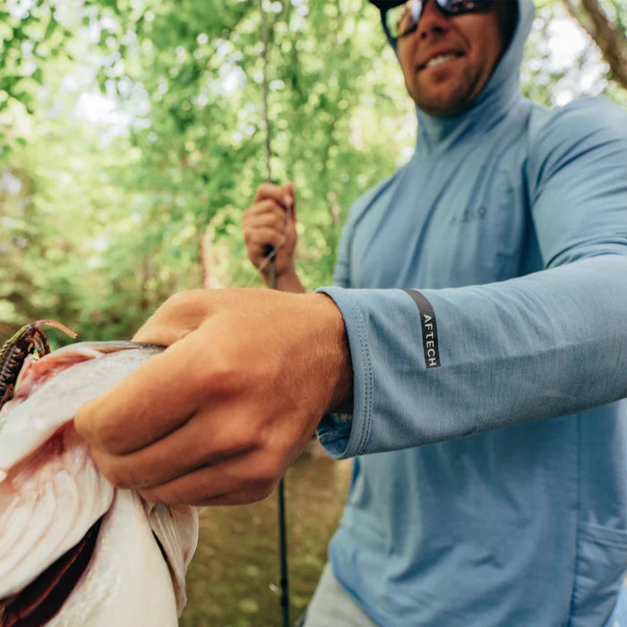 Person holding a fish outdoors with a blurred natural background