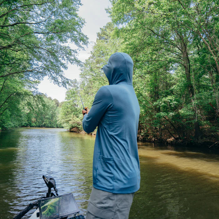 Person fishing from a boat on a river surrounded by trees