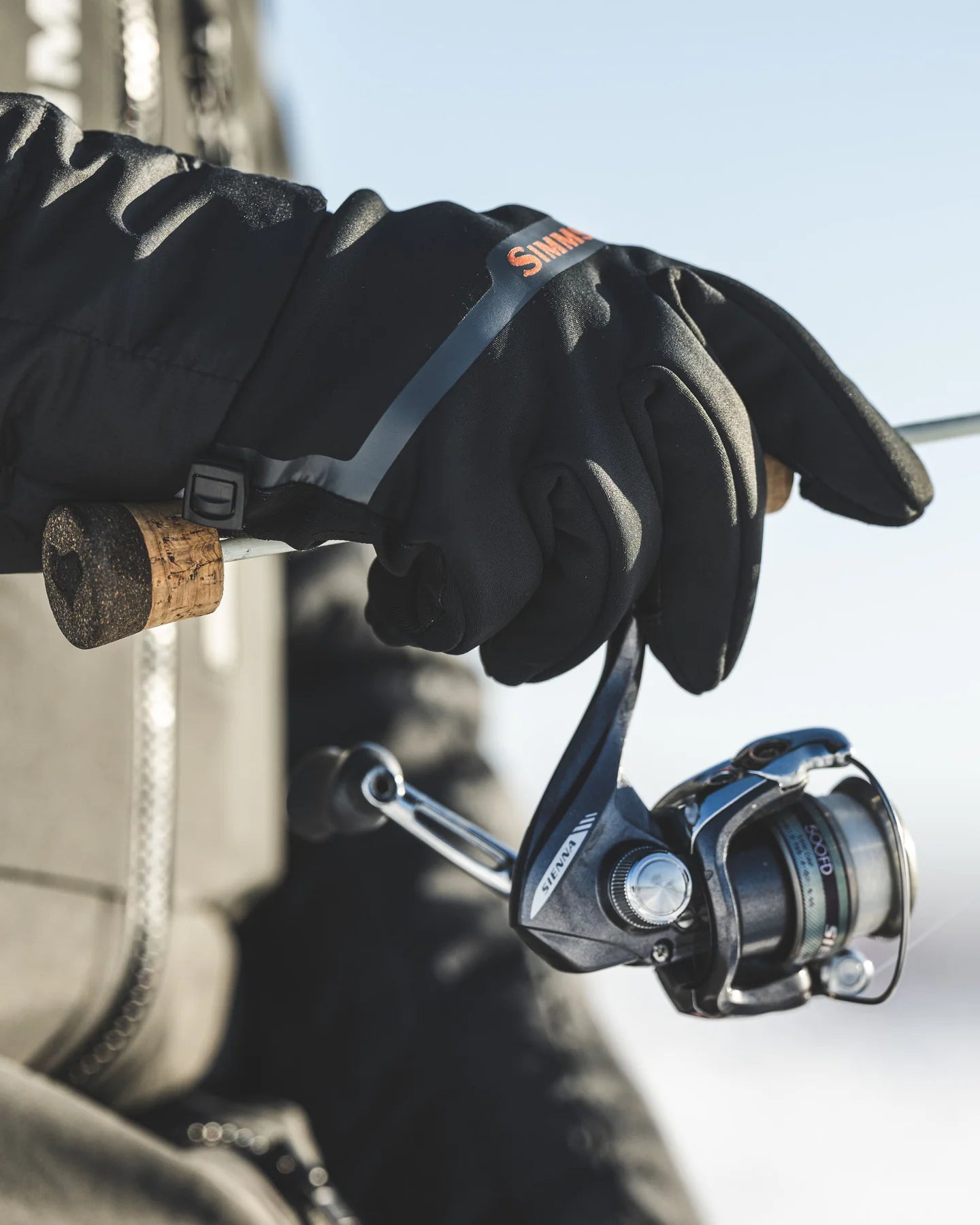 Person wearing black gloves holding a fishing reel with a blurred background
