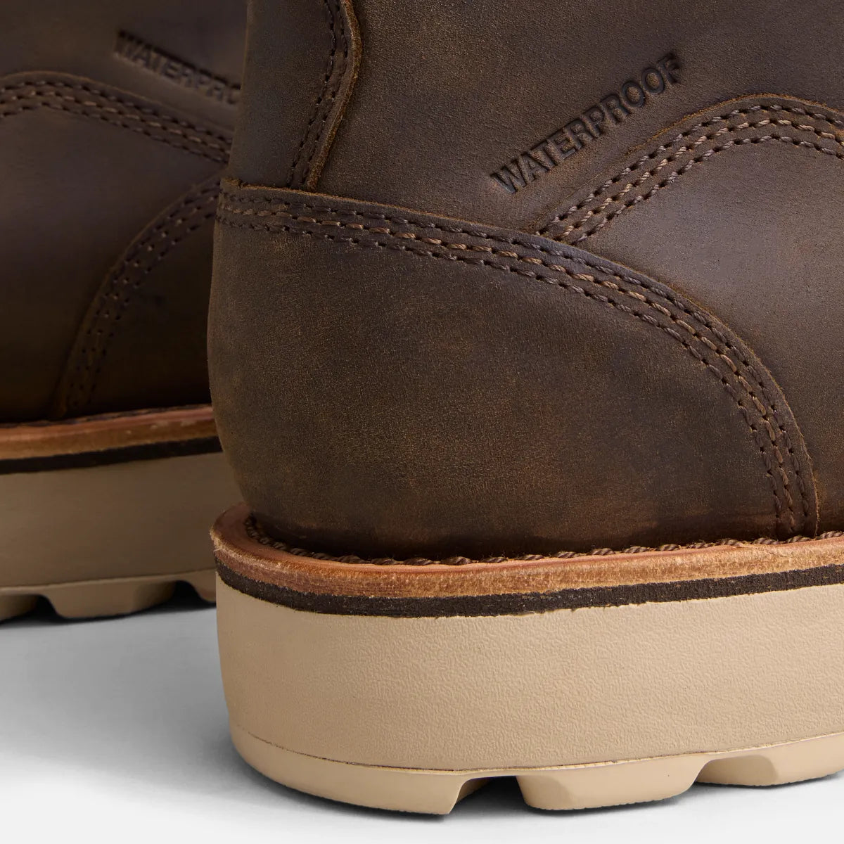 Close-up of brown leather boots with 'Waterproof' label on a light gray background