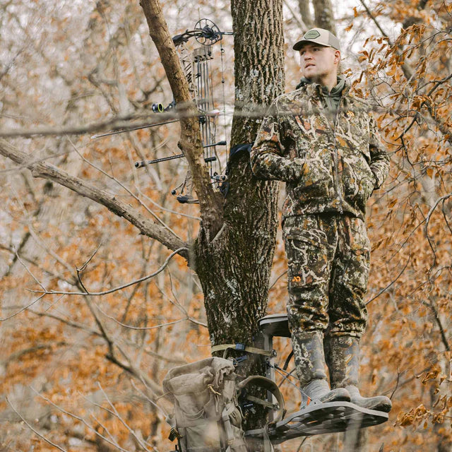 Hunter in camouflage gear using a tree stand in a forest during autumn.