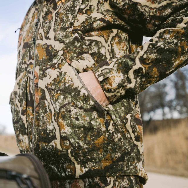 Camouflage-patterned jacket with a visible brand logo on a blurred natural background