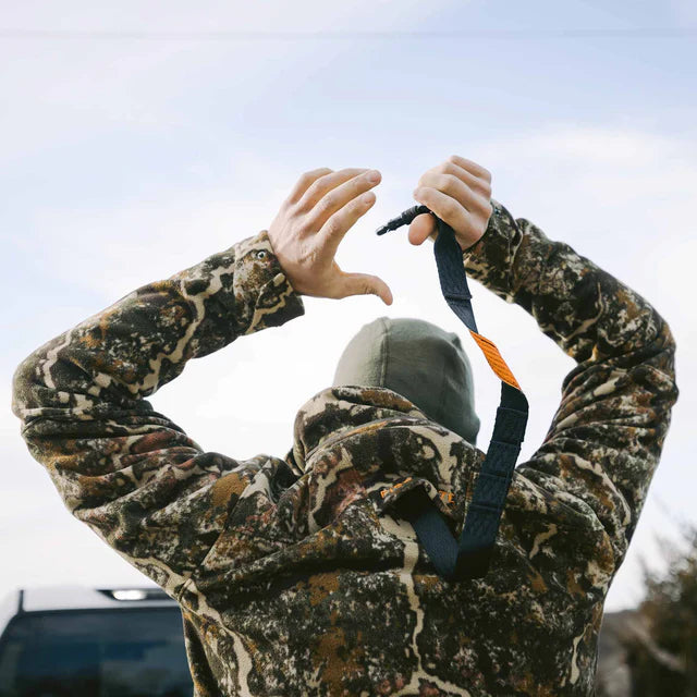 Person in camouflage jacket holding a bow with a clear sky background