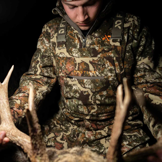 Person in camouflage hunting gear holding deer antlers against a dark background