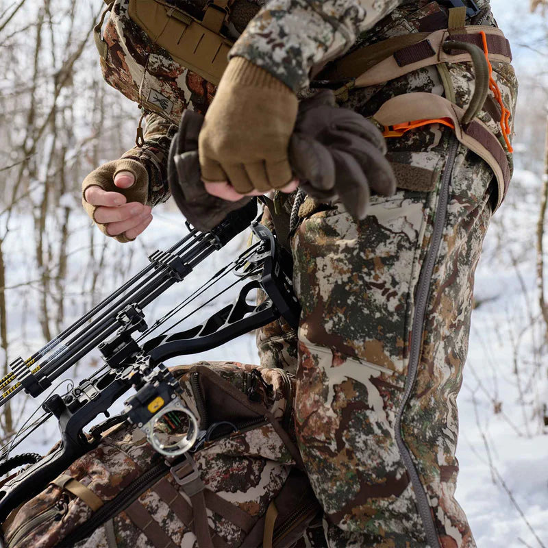 Person in camouflage gear holding a crossbow in a snowy forest setting
