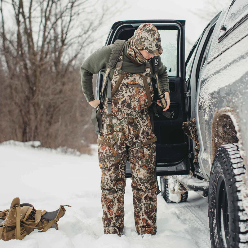 Person in full camouflage gear getting into a snow-covered vehicle