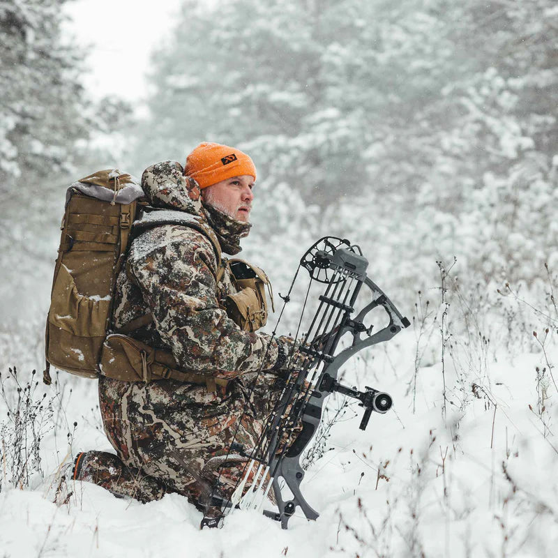 Hunter in camouflage gear with a bow in a snowy forest