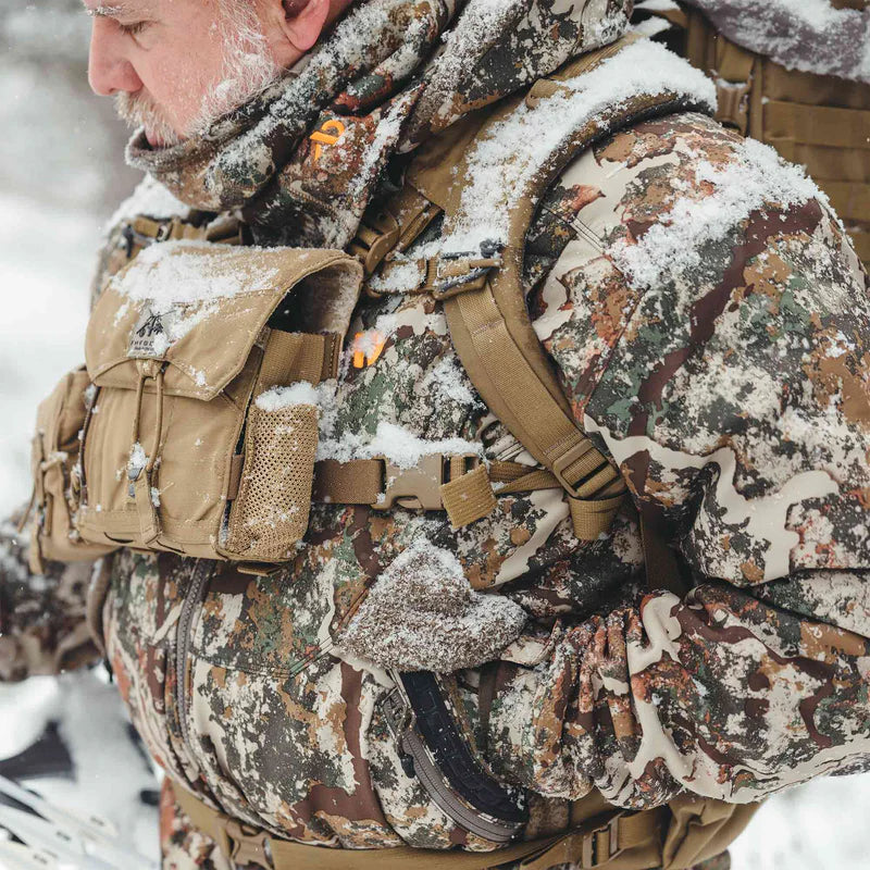 Person in full camouflage hunting gear with a backpack in a snowy environment