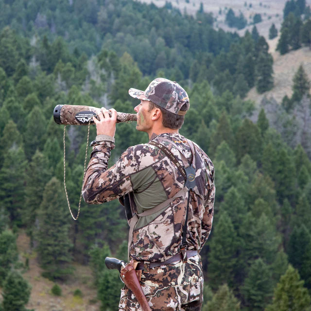 Hunter in camouflage clothing using a binoculars in a forested area