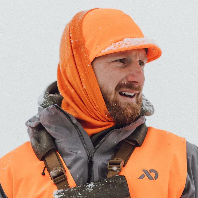 Person wearing an orange hood and safety vest in a snowy environment
