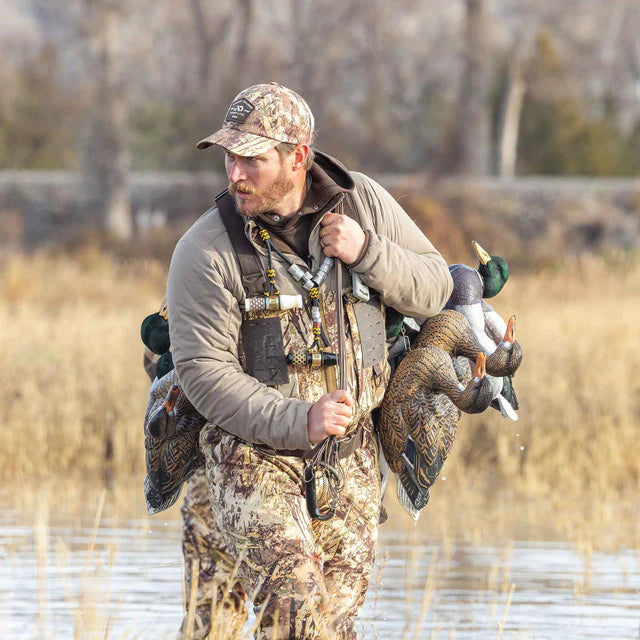 Man in camouflage clothing carrying dead ducks in a field