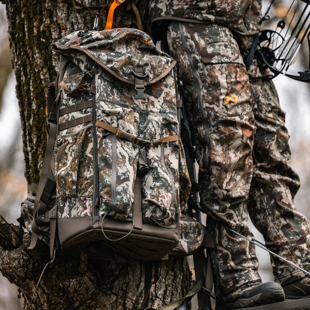 Person in camouflage gear with a backpack on a tree branch