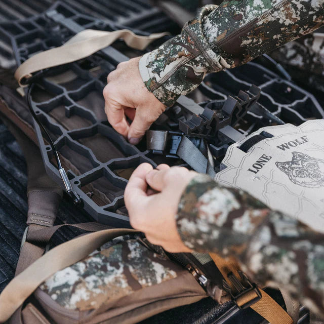 Person in camouflage gear adjusting a hunting blind with 'Lone Wolf' branding.