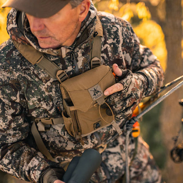 Man in camouflage hunting gear holding a tactical pouch in a forest setting