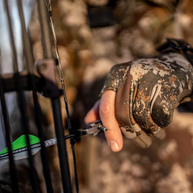 Hand wearing a camouflage glove holding a bow with a blurred natural background