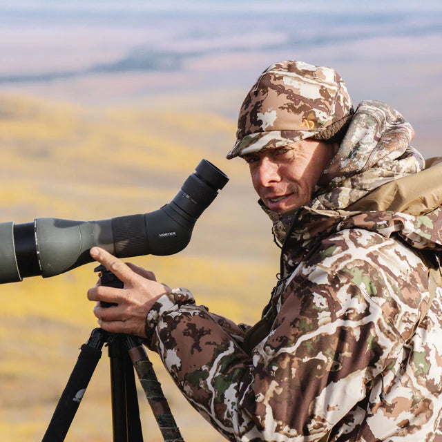 Person in camouflage gear using a spotting scope in a natural setting