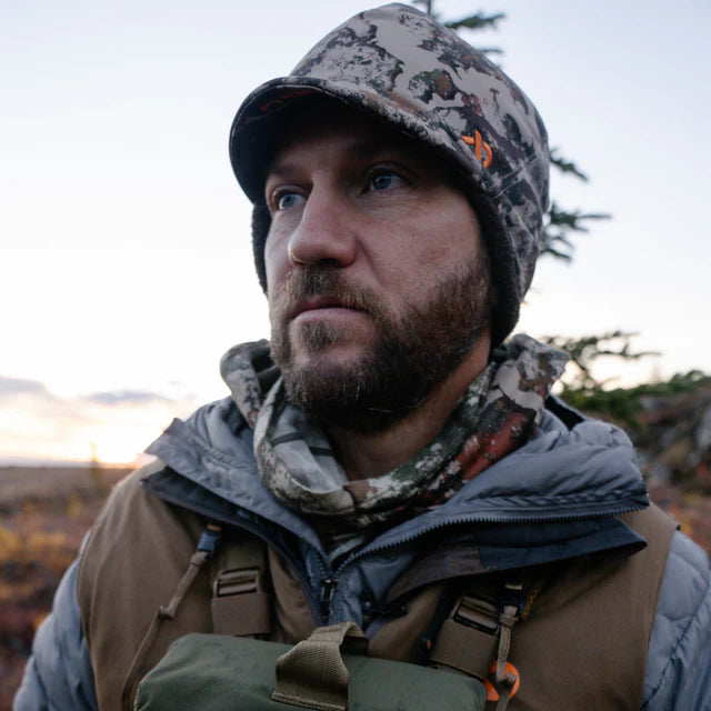 Man wearing camouflage clothing and a hat in an outdoor setting